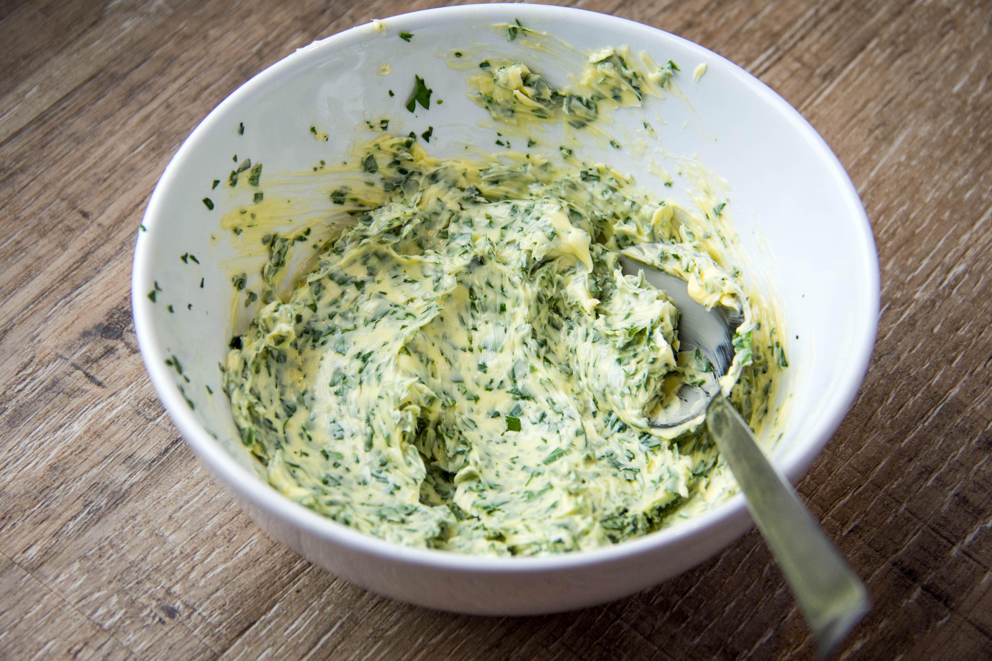 Bowl of softened lemon and herb butter for roast chicken, showing the mixture before it is worked under the skin.